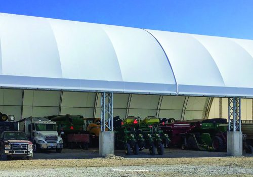 Vehicles are seen under a protective fabric structure. Greenfield Contractors builds storage buildings for transportation.